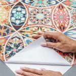 Close-up of colourful patterned peel and stick wallpaper being peeled back to show the adhesive backing.