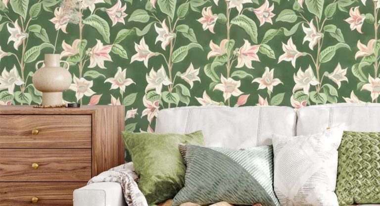 A moonflower themed green wallpaper on a wall with a couch with cushions and a side table with a lamp infront of it