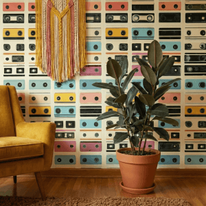 A zoomed-in of a retro cassette wallpaper, showcasing pastel mixtape designs, a mustard armchair, and warm wood accents.