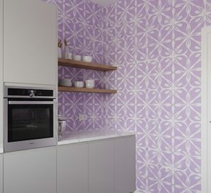Lilac geometric petal wallpaper on a kitchen wall with built-in oven, floating shelves, and minimalist white finishes